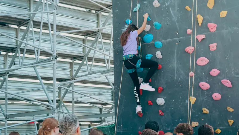Una bambina scala la parete di arrampicata sportiva